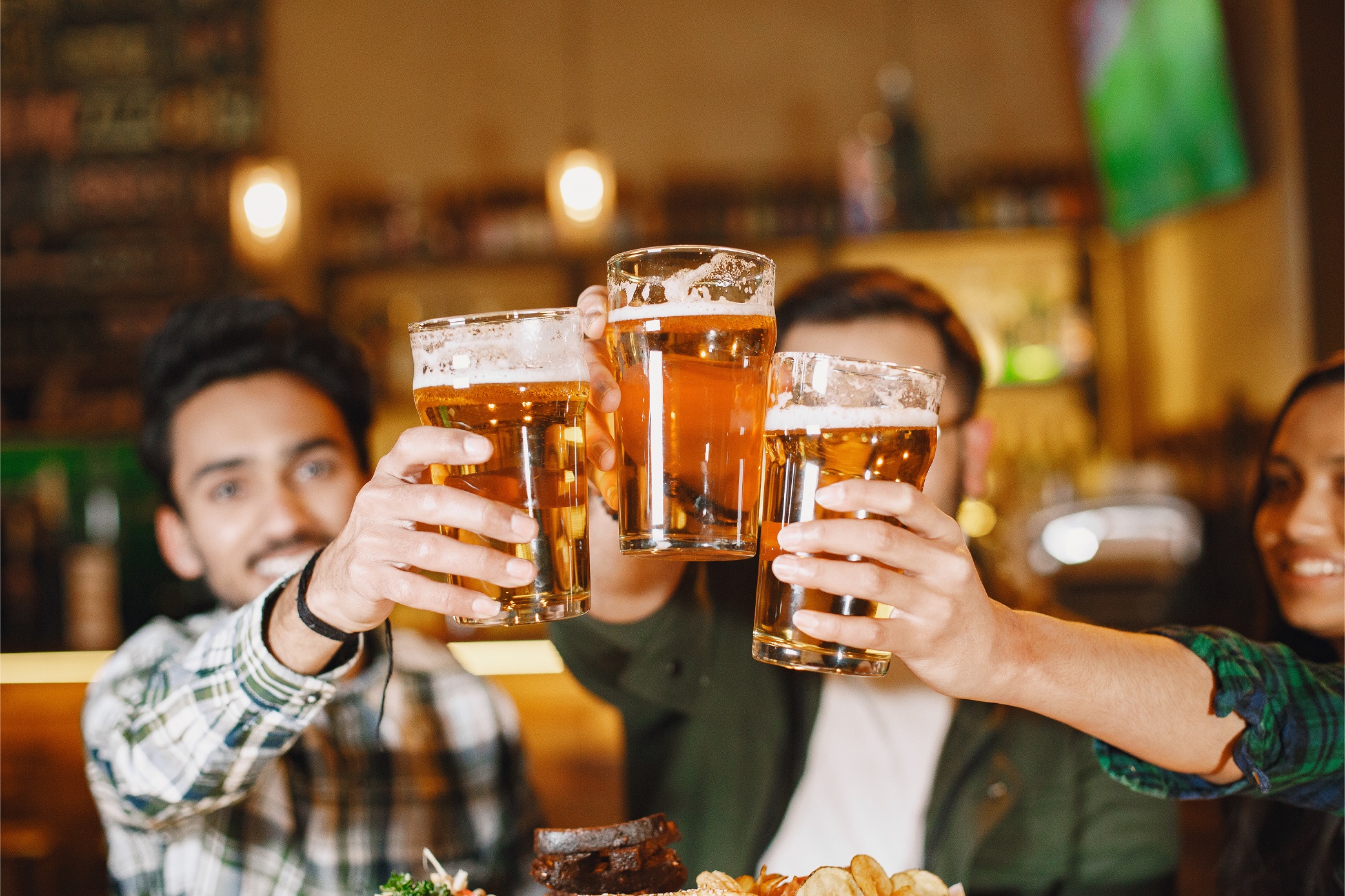 Drei Personen stoßen mit einem Bier an.